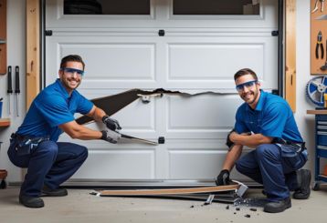 Two professional technicians in blue uniforms repairing a broken white garage door panel inside a Savage, MN garage