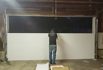 Technician installing lower panels of a new sectional garage door inside Snyder home garage